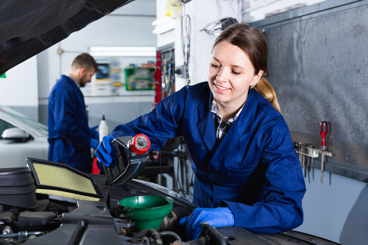 Jonge vrouw vult olie bij in auto.